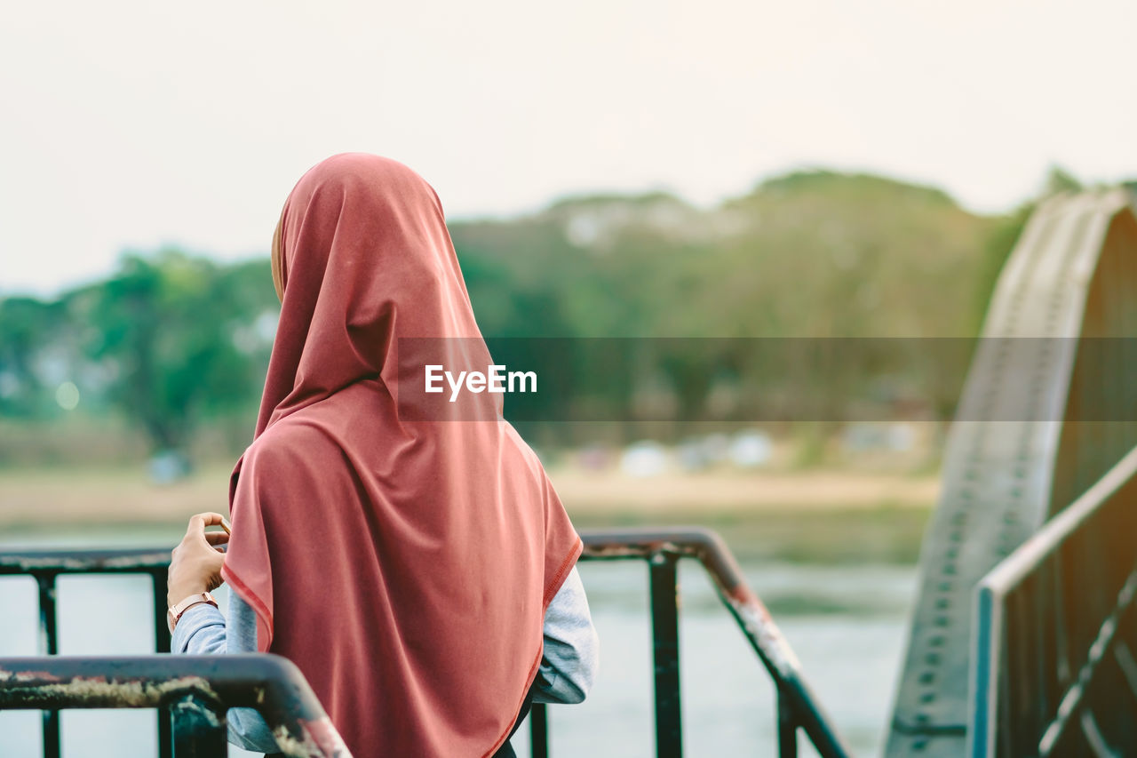 REAR VIEW OF WOMAN SITTING ON RAILING