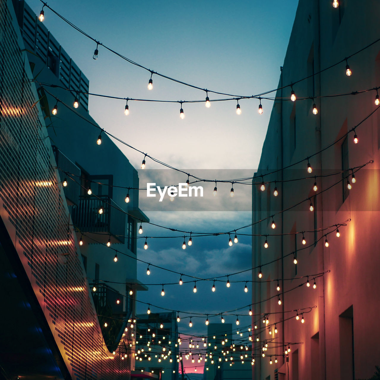 Low angle view of illuminated light bulbs amidst building against sky at night