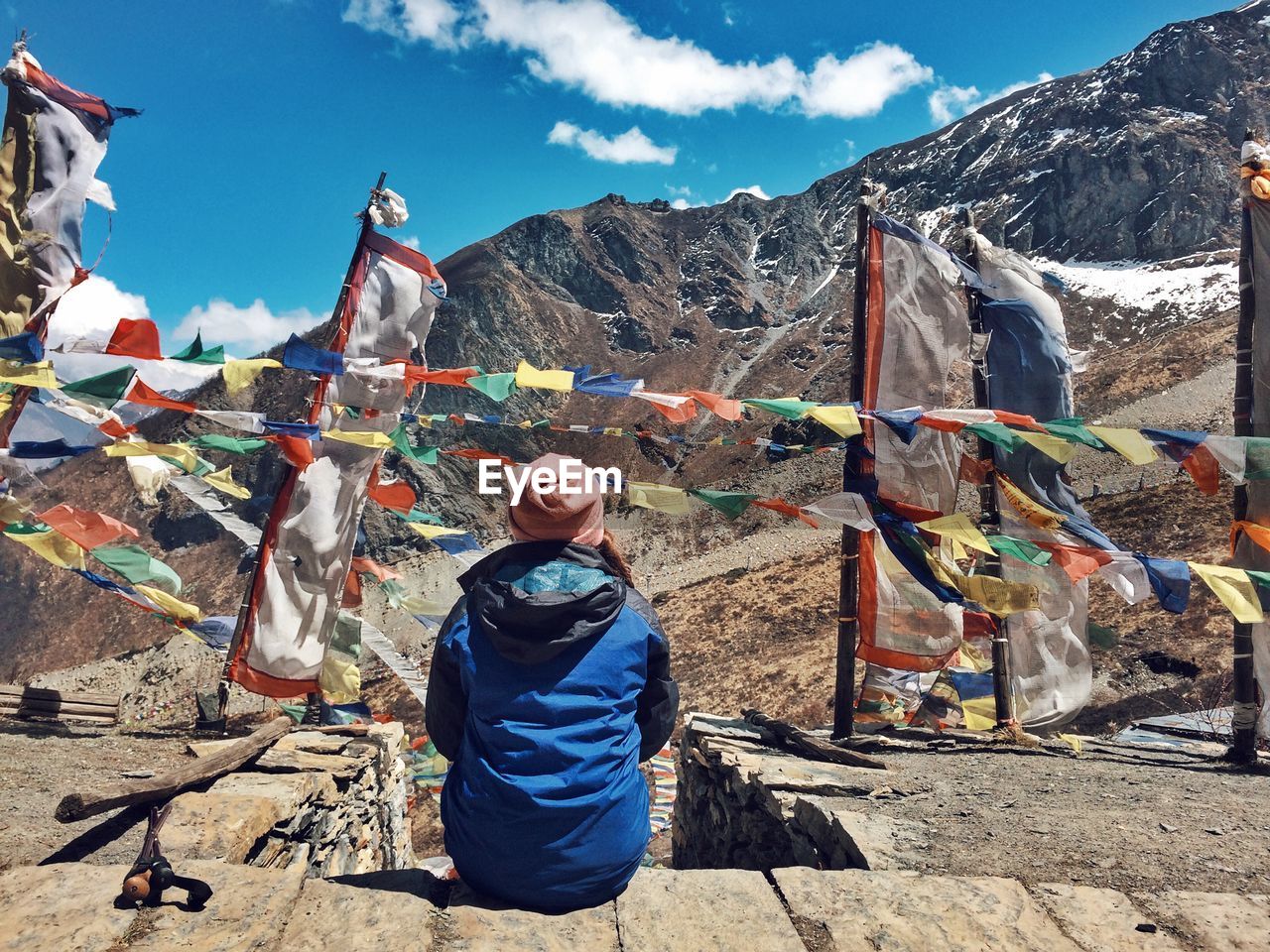 Rear view of woman looking at mountains while sitting by prayer flags