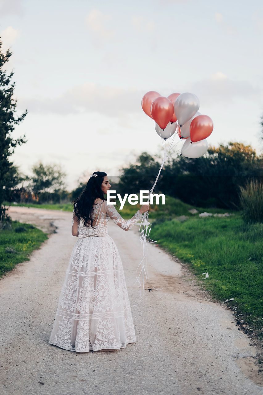 REAR VIEW OF WOMAN WITH BALLOONS AT ROAD