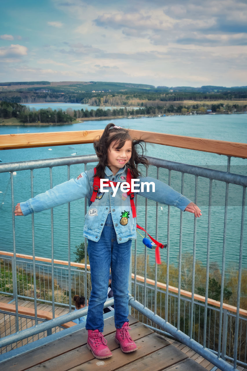 Full length of girl standing by railing against sea