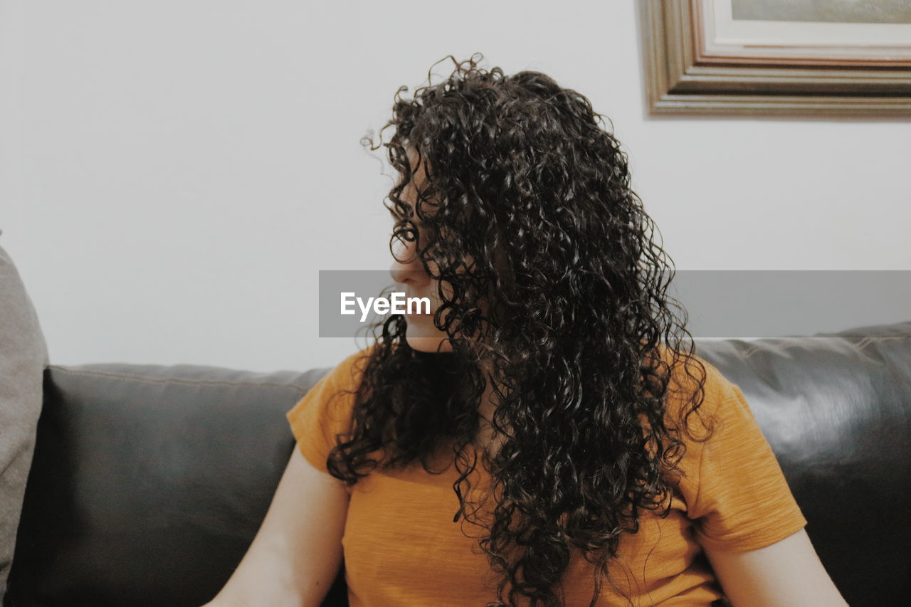 Woman with curly hair sitting on sofa at home