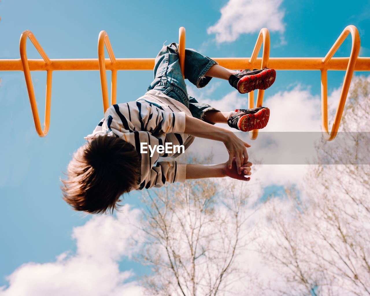 Low angle view of boy playing on monkey bars against sky