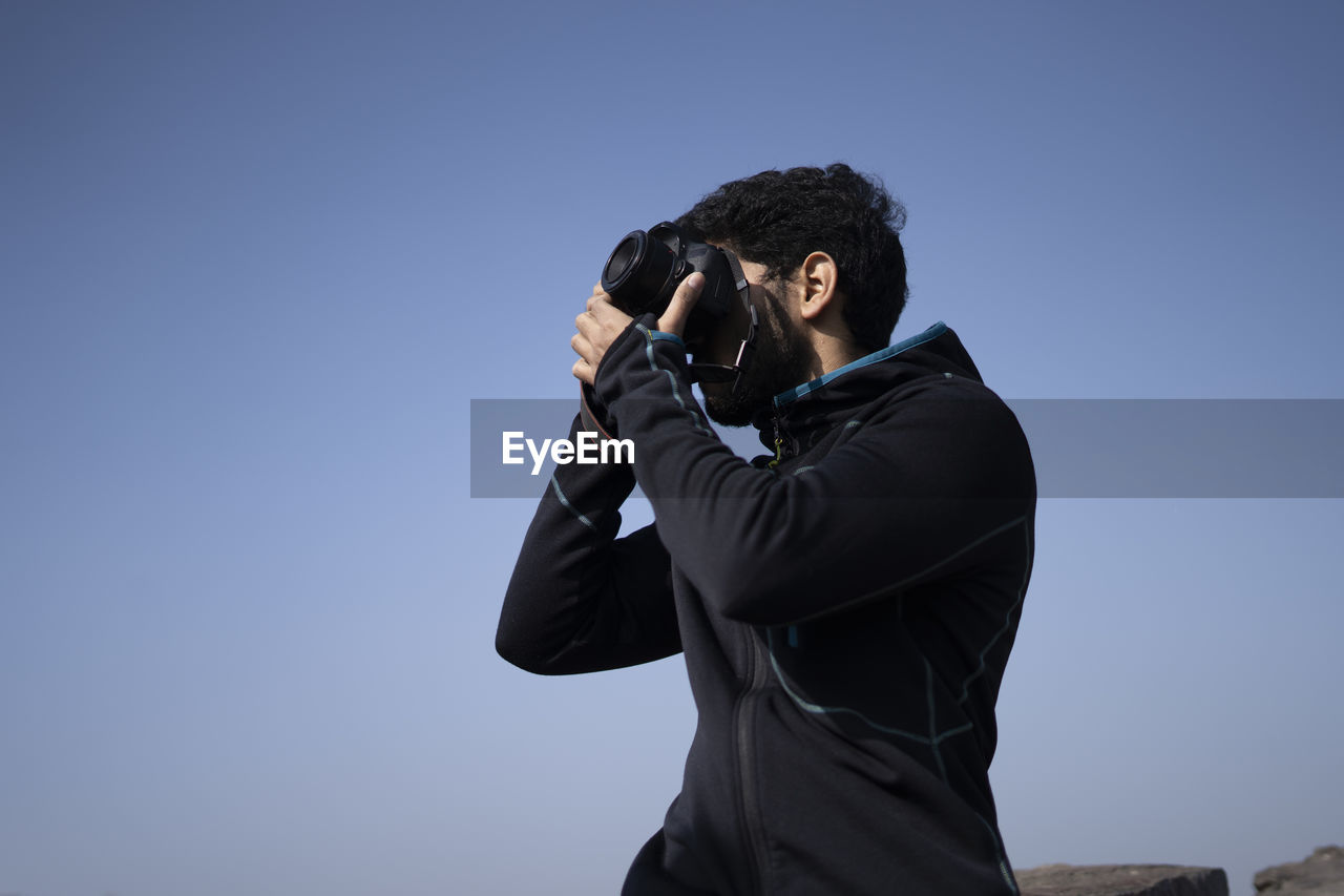 YOUNG MAN PHOTOGRAPHING AGAINST SKY