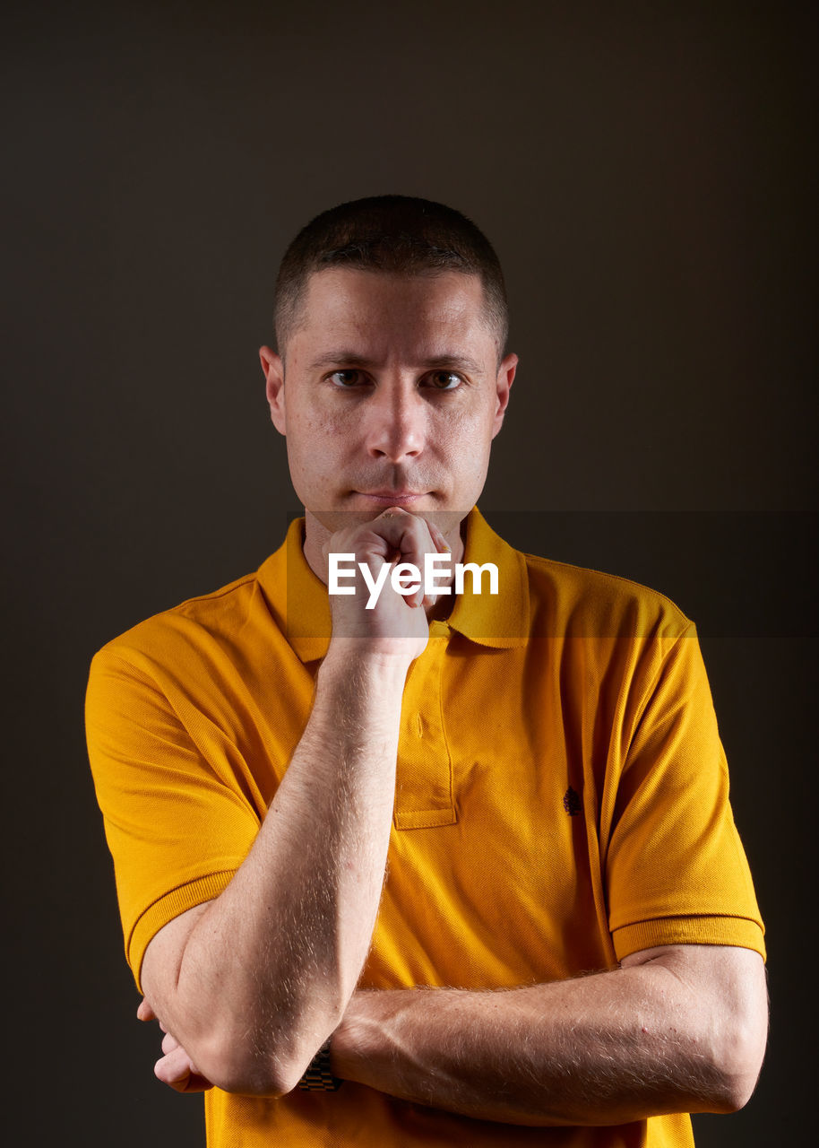 studio shot, one person, yellow, adult, men, portrait, indoors, young adult, person, black background, emotion, looking at camera, waist up, front view, facial expression, casual clothing, lifestyles, arm, sports, serious, hand