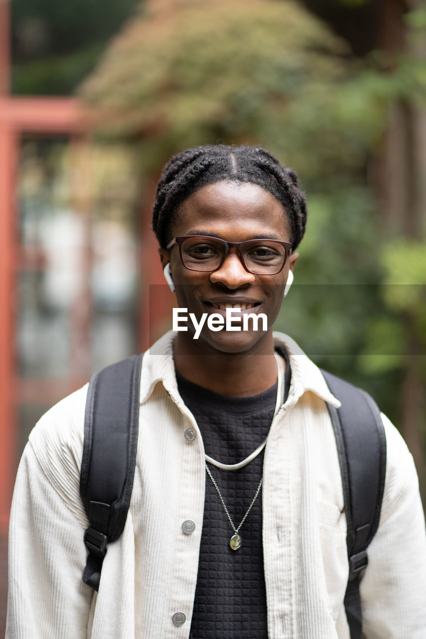 Cheerful african guy student in glasses smiling at camera, standing near university campus outdoors