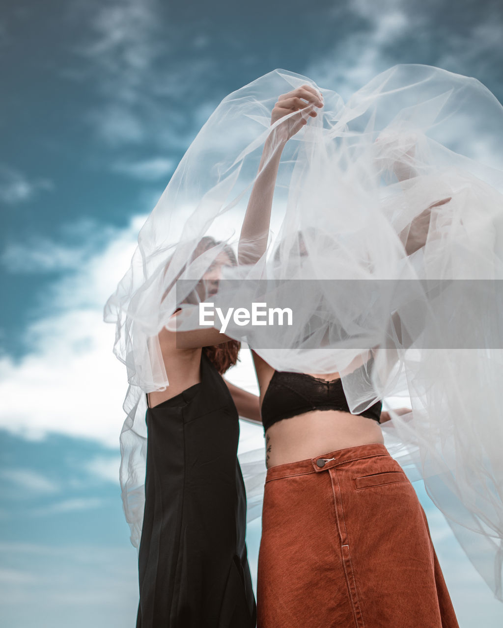 MIDSECTION OF WOMAN HOLDING UMBRELLA AGAINST WHITE SKY
