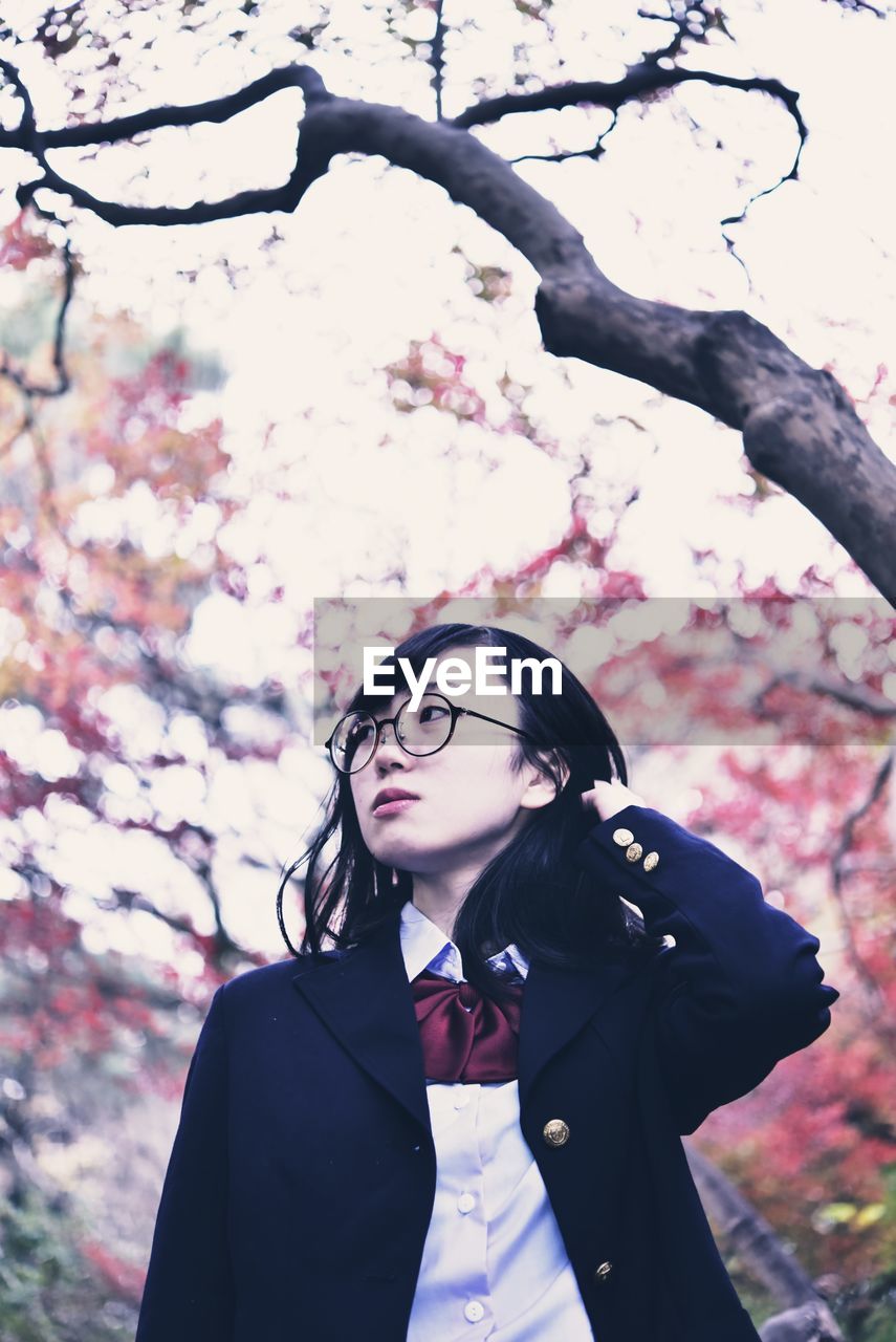 Woman looking away while standing against tree