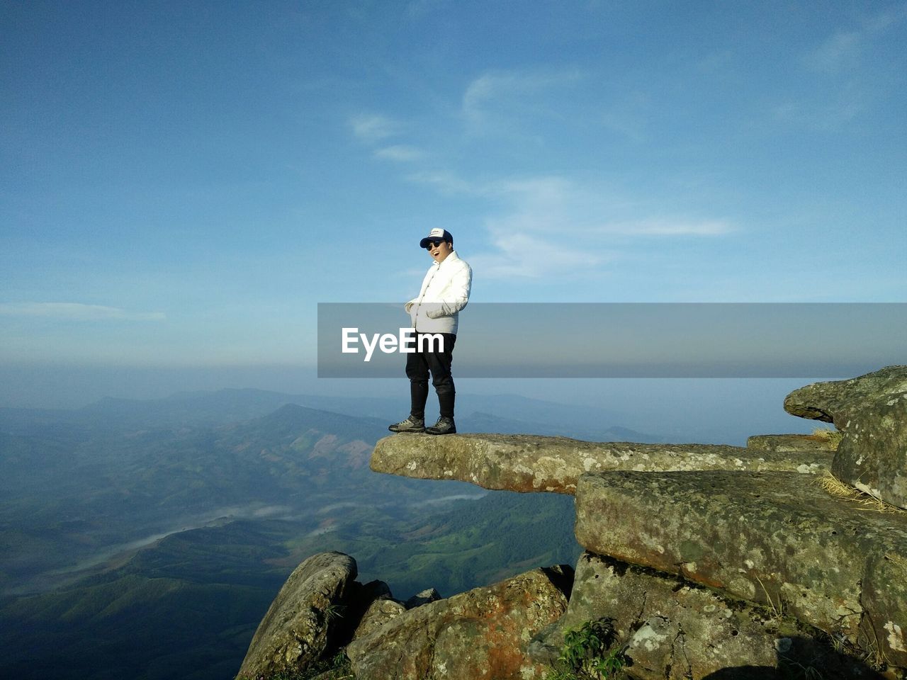 Side view of man sitting on cliff against sky