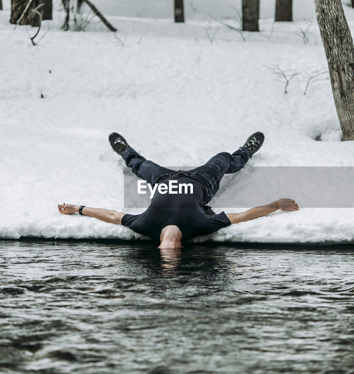 Man lies on back in snow spread eagle with head underwater in river person
