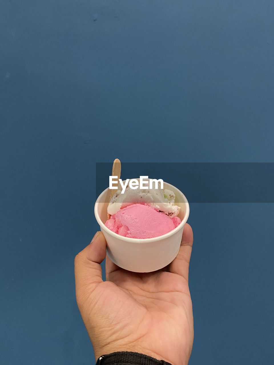 hand, finger, holding, food and drink, one person, food, adult, fashion accessory, copy space, sweet food, sweet, studio shot, indoors, blue background, blue, freshness, arm, limb, pink, close-up