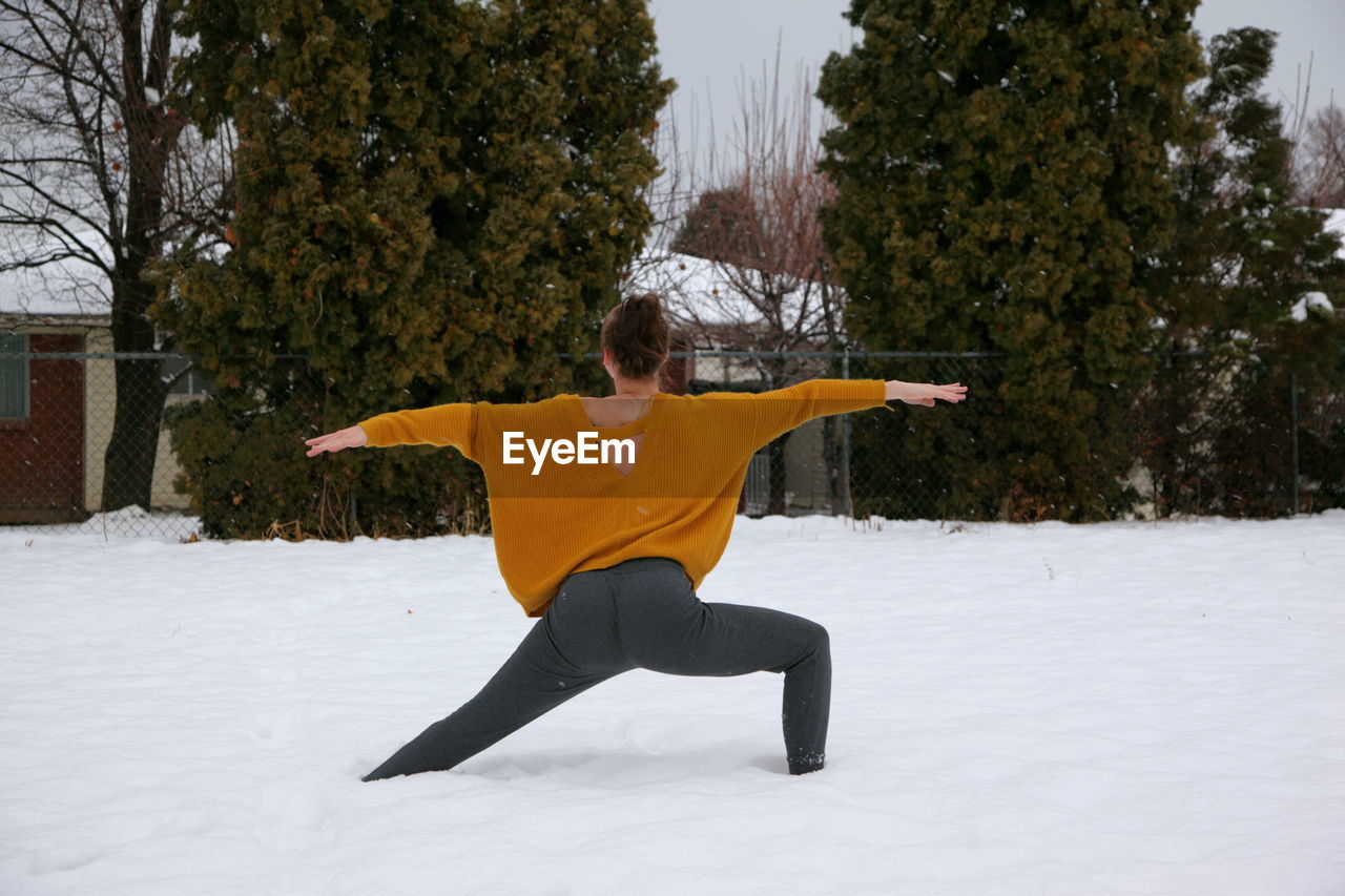 Rear view of young woman exercising on snow covered field