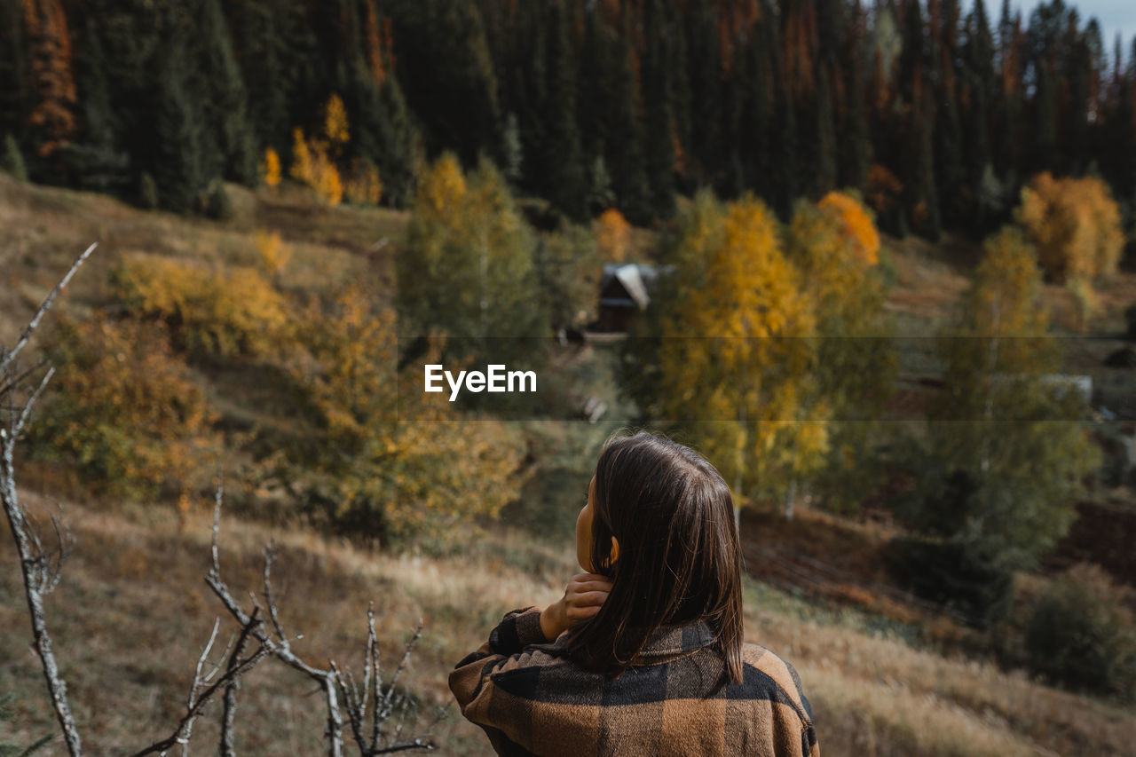 Rear view of woman standing amidst trees in forest during autumn