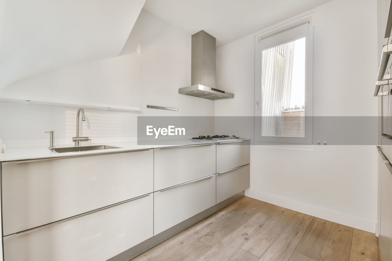 Modern chrome hood and built in oven in contemporary light kitchen with white cabinets