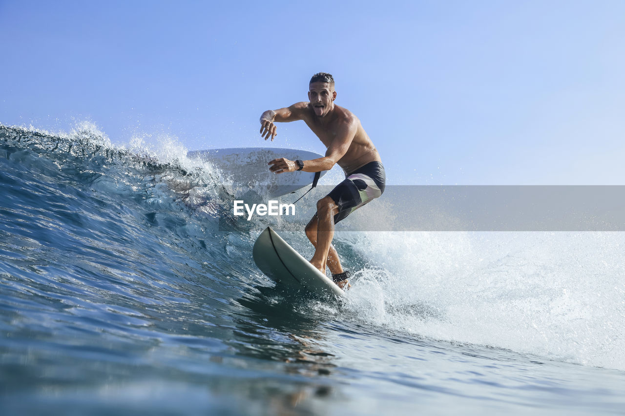 Man balancing while surfing in sea against clear sky