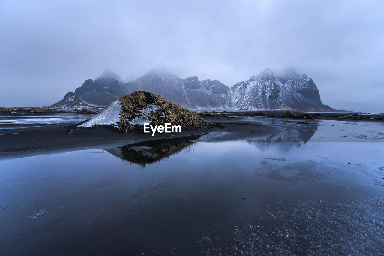 Picturesque nordic scenery of snowy rocky formations surrounded by frozen sea during overcast foggy day