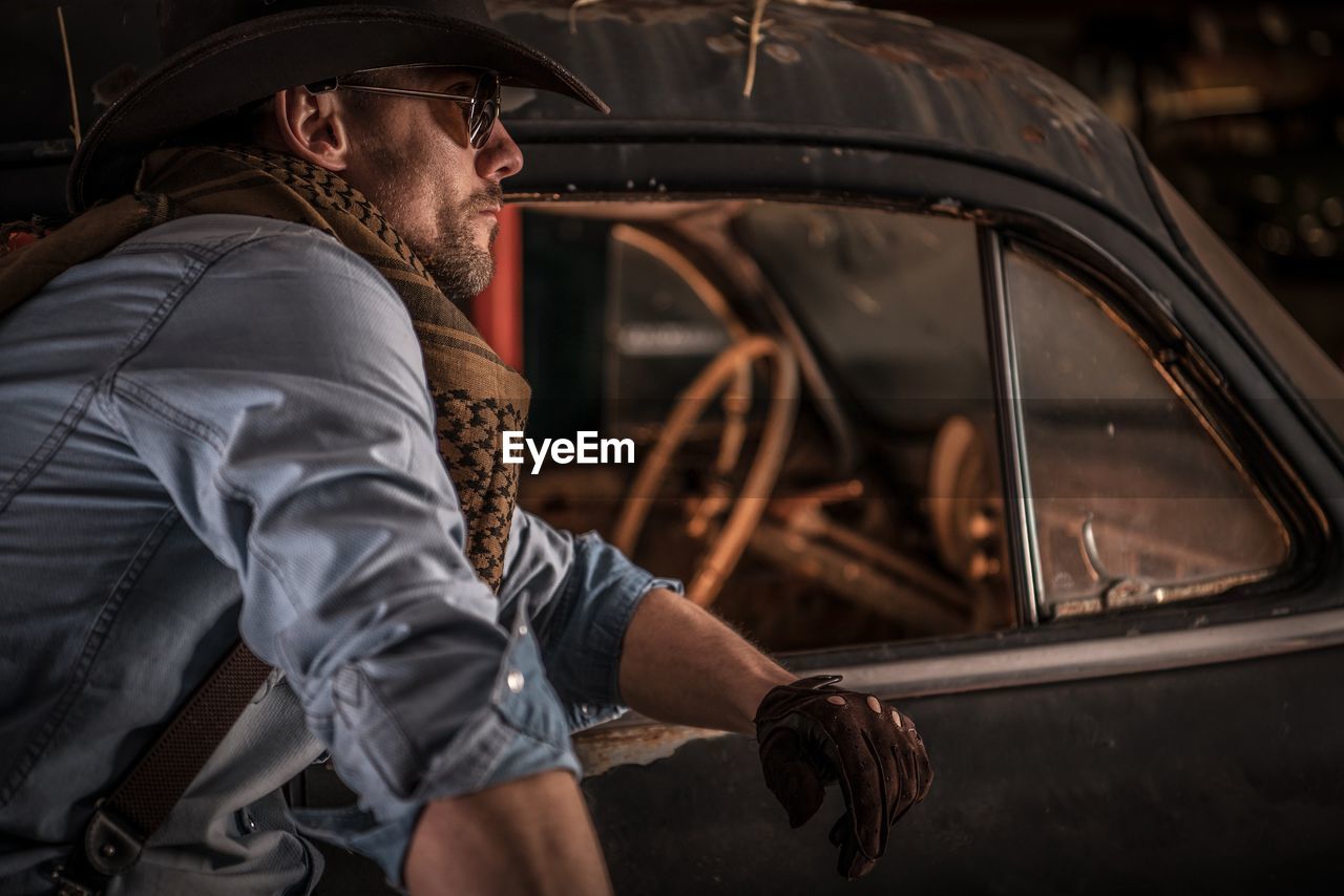 Side view of mid adult man standing by abandoned car