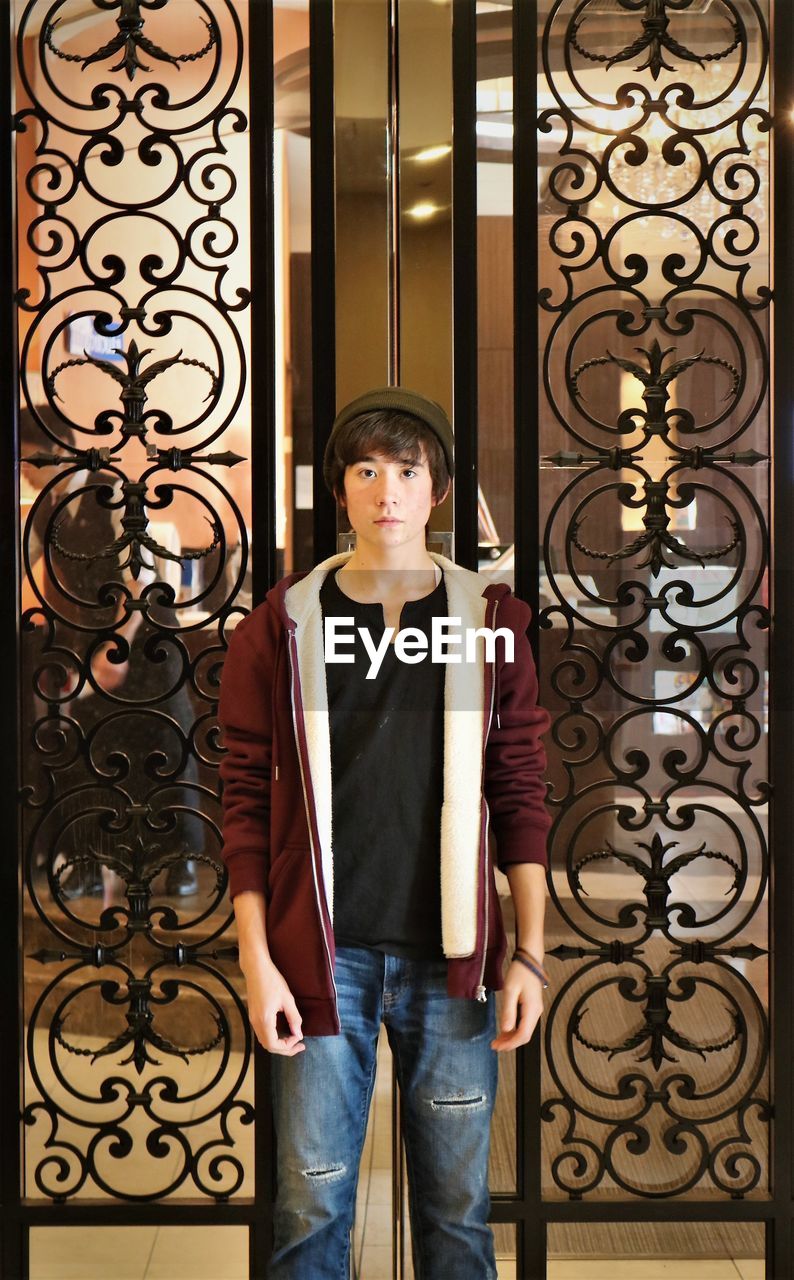 Portrait of teenage boy standing against wrought iron