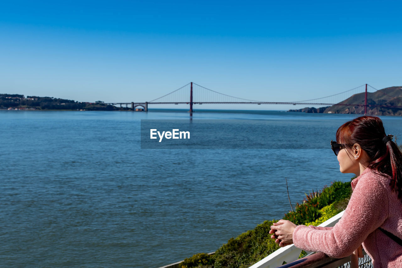 MAN LOOKING AT SUSPENSION BRIDGE OVER RIVER