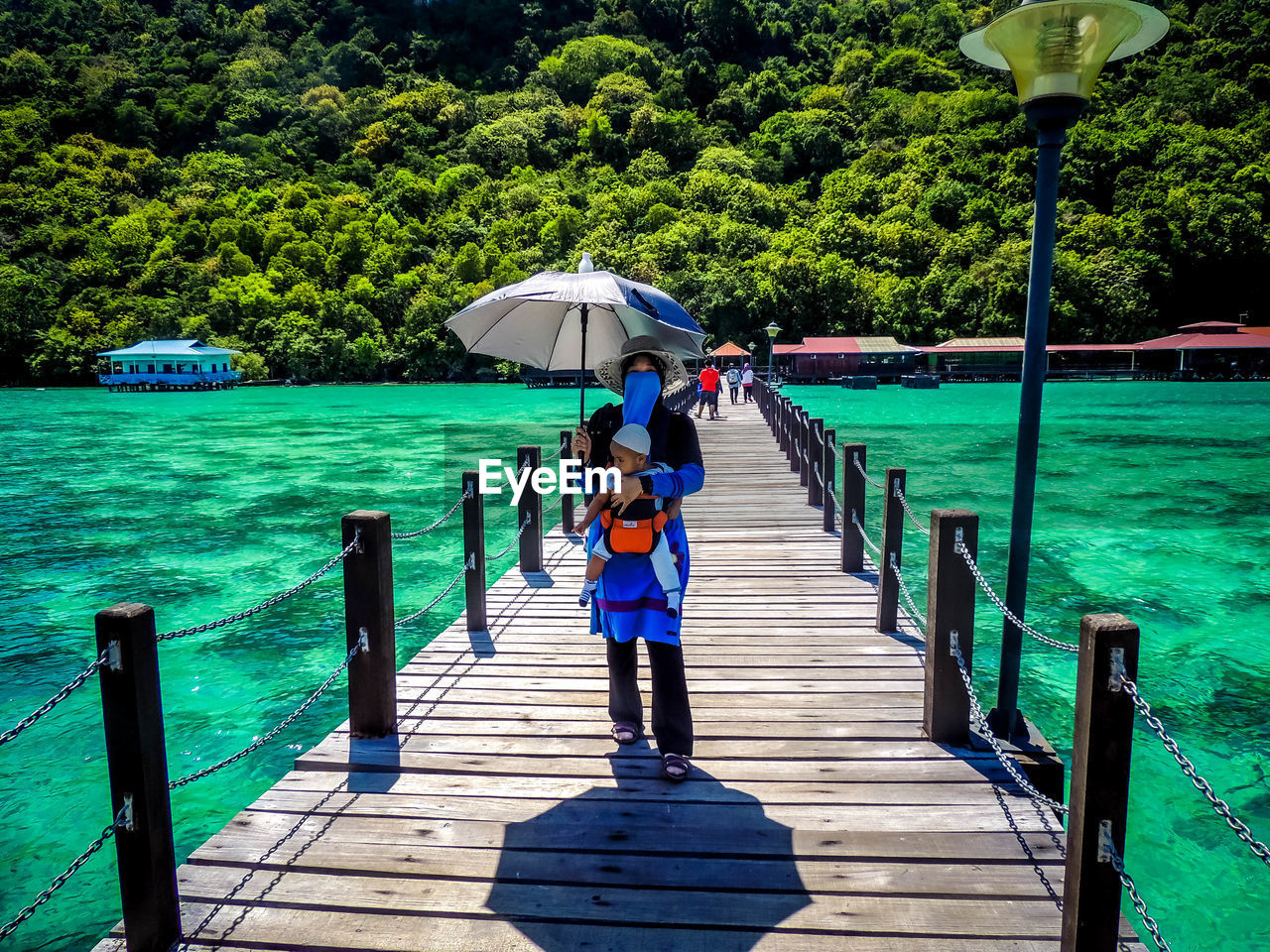 REAR VIEW OF WOMAN WALKING ON FOOTBRIDGE BY WATER