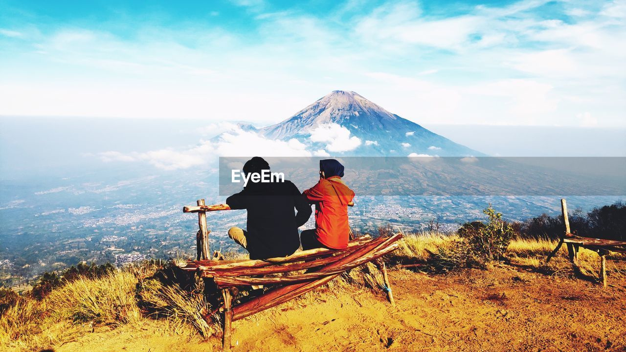 REAR VIEW OF MEN LOOKING AT MOUNTAINS