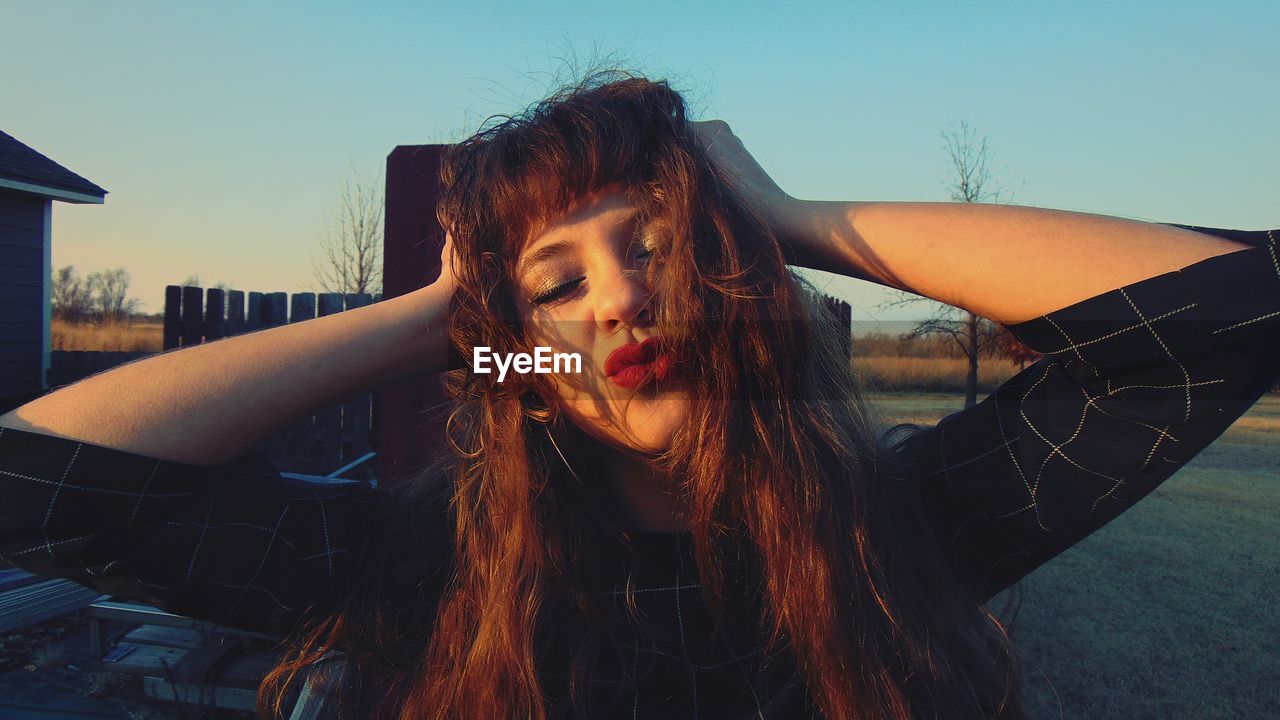 Close-up of young woman puckering against sky during sunset