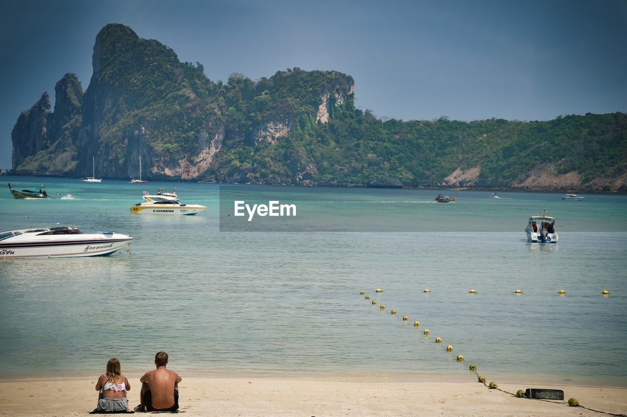 PEOPLE ON BEACH AGAINST MOUNTAINS