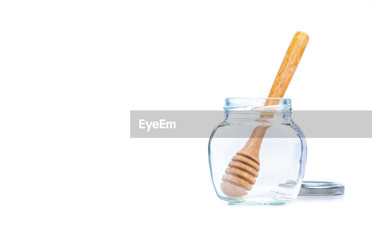 Wooden honey dipper inside empty glass jar on white background