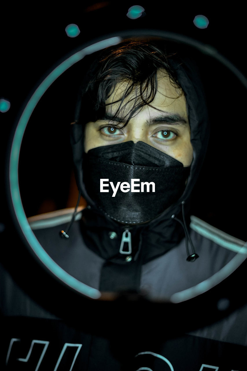 Close-up portrait of masked man against black background