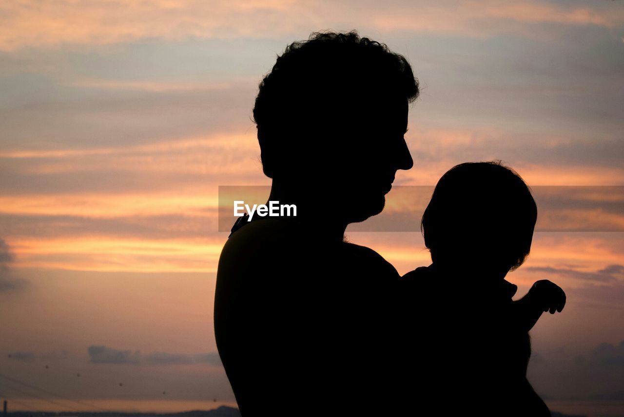 Silhouette father carrying son against sky at sunset