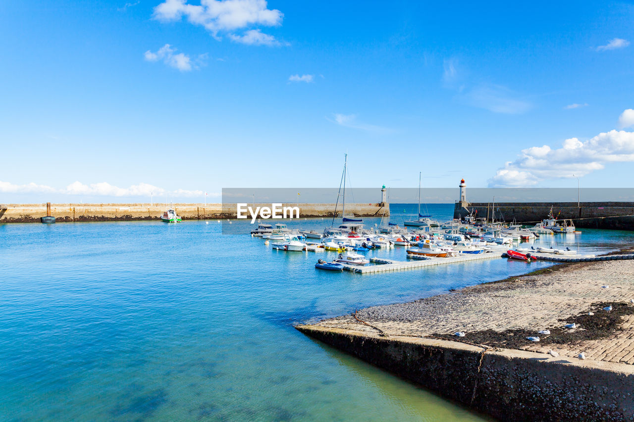 Sailboats moored in sea against blue sky