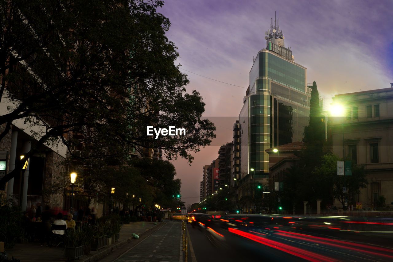 LIGHT TRAILS ON ROAD AMIDST BUILDINGS IN CITY