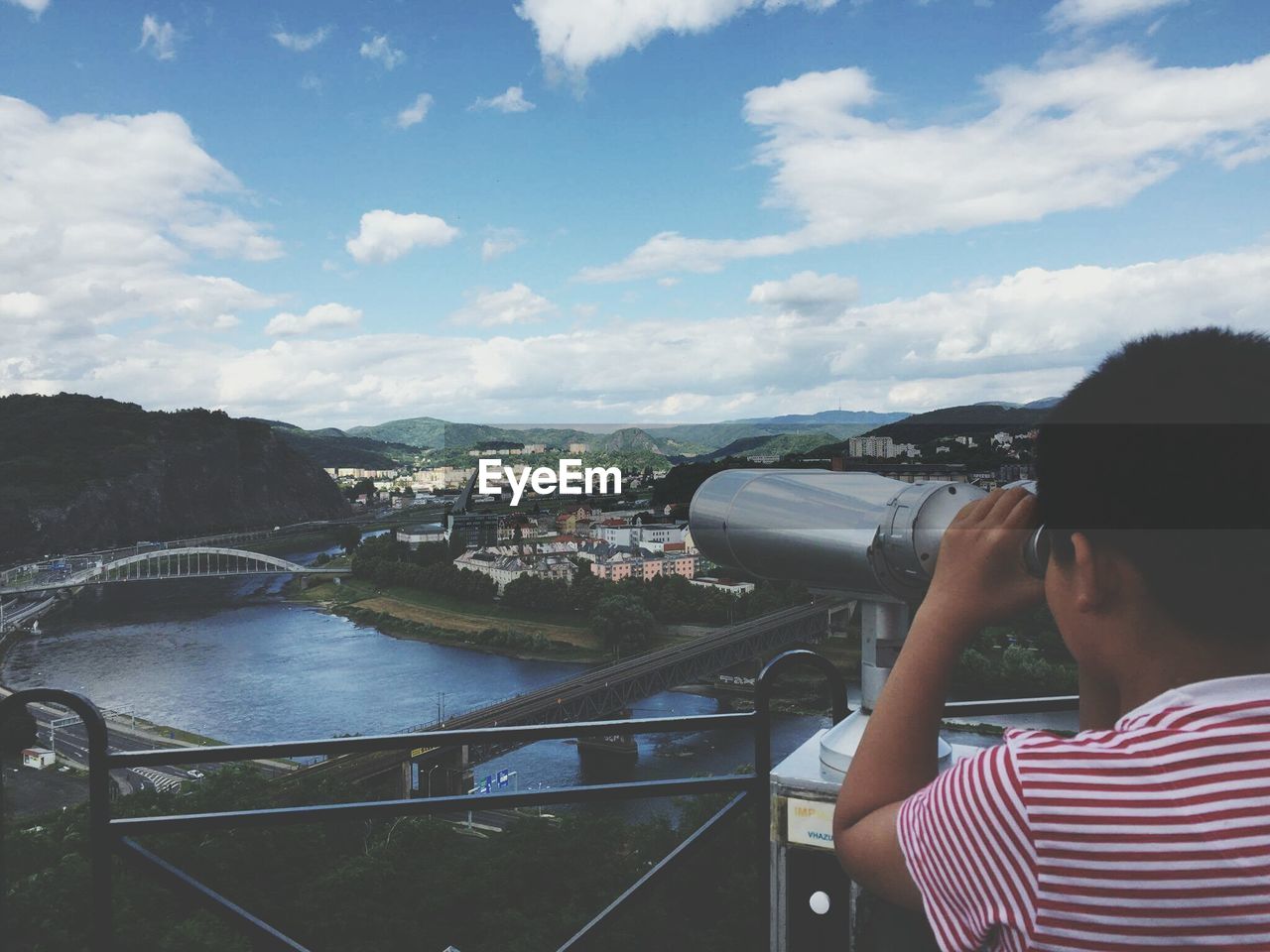Boy looking through coin-operated binoculars at observation point by river