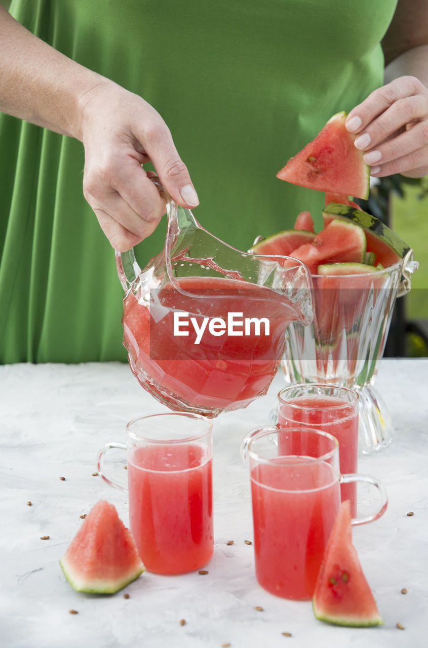 Young woman in a green dress pours a red refreshing drink from watermelon pulp into a glass 