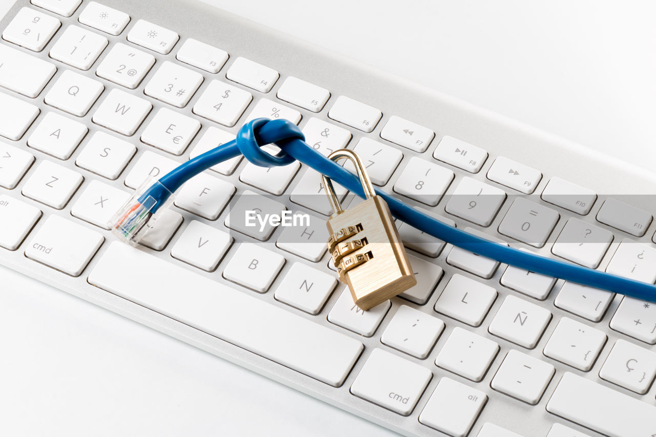 High angle view of padlock and cable on computer keyboard against white background
