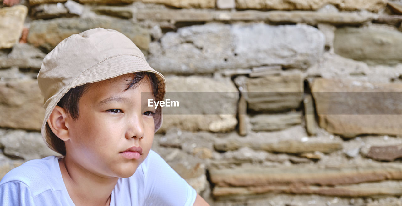 PORTRAIT OF BOY LOOKING AT STONE WALL