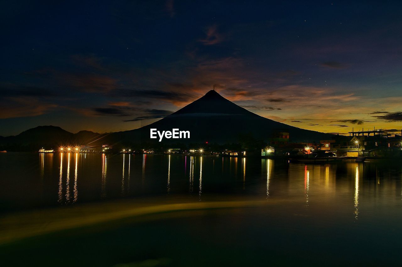 ILLUMINATED BUILT STRUCTURES BY SEA AGAINST SKY AT NIGHT