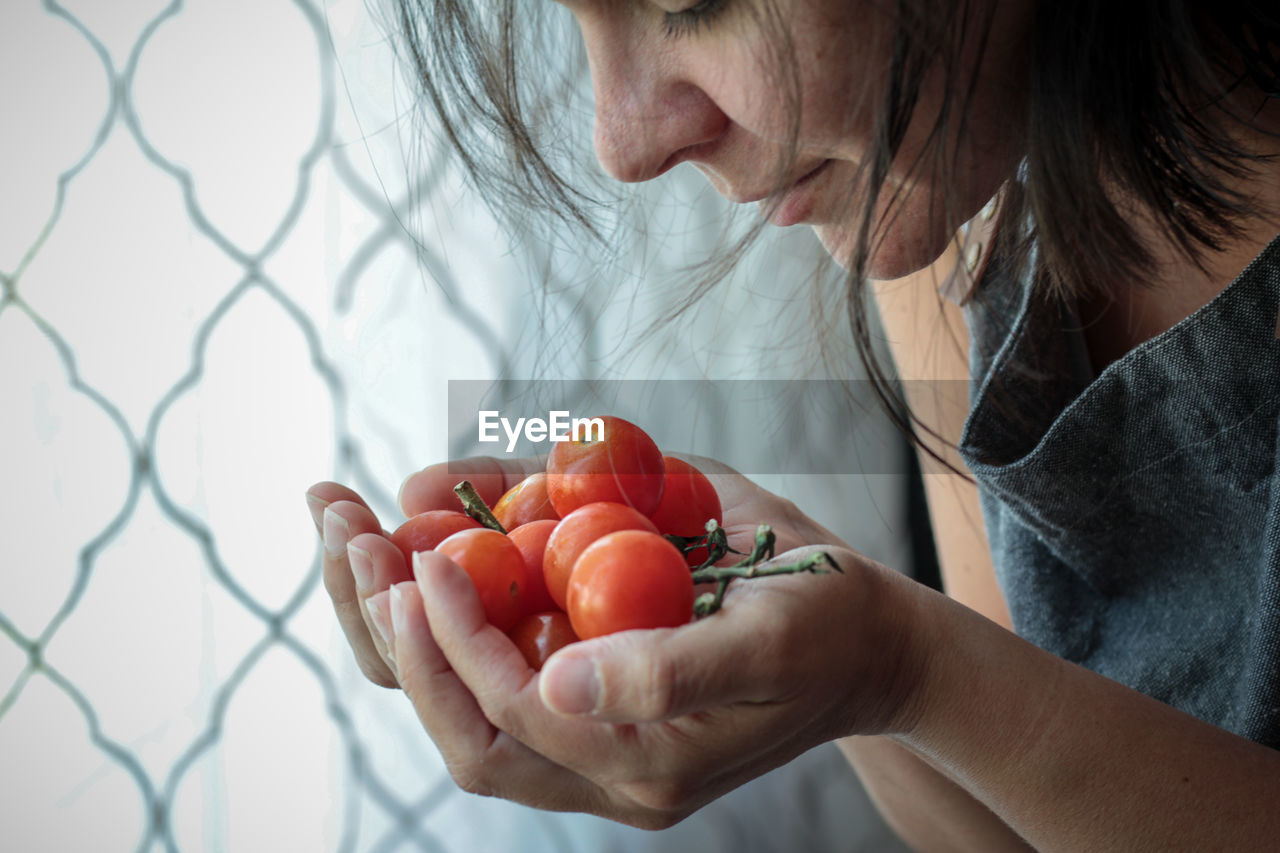 Woman smelling fresh cherry tomatoes against window 