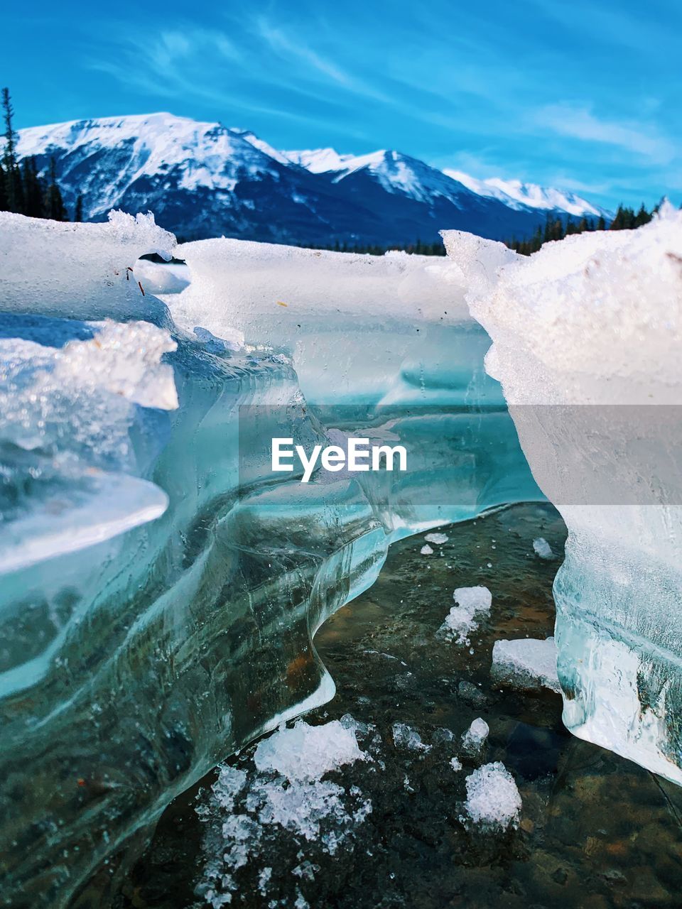 Low angle shot of a crack in the melting ice of frozen lake with mountains in the distance