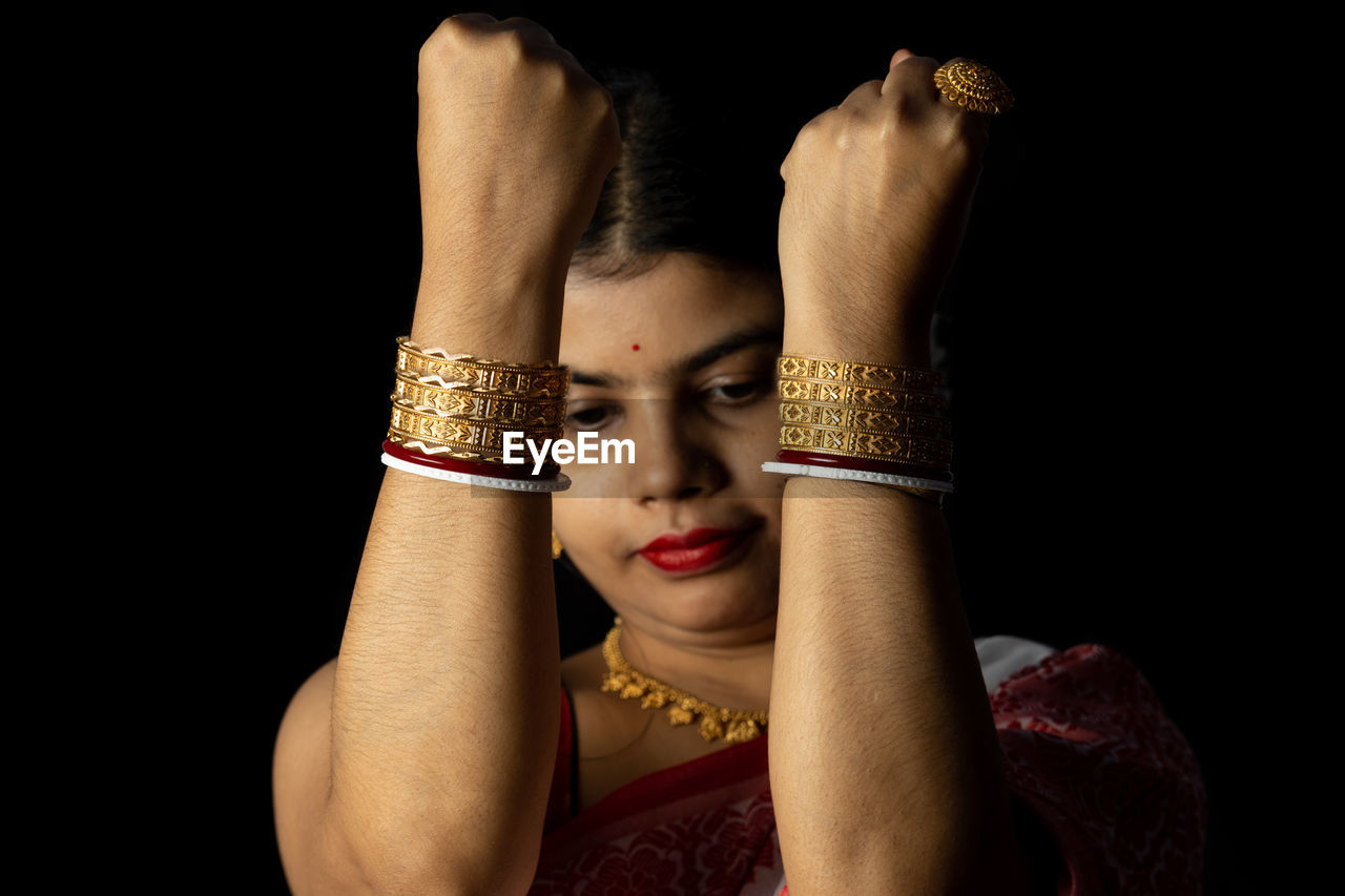 An indian woman in red saree wearing bangles with smiling face on black background