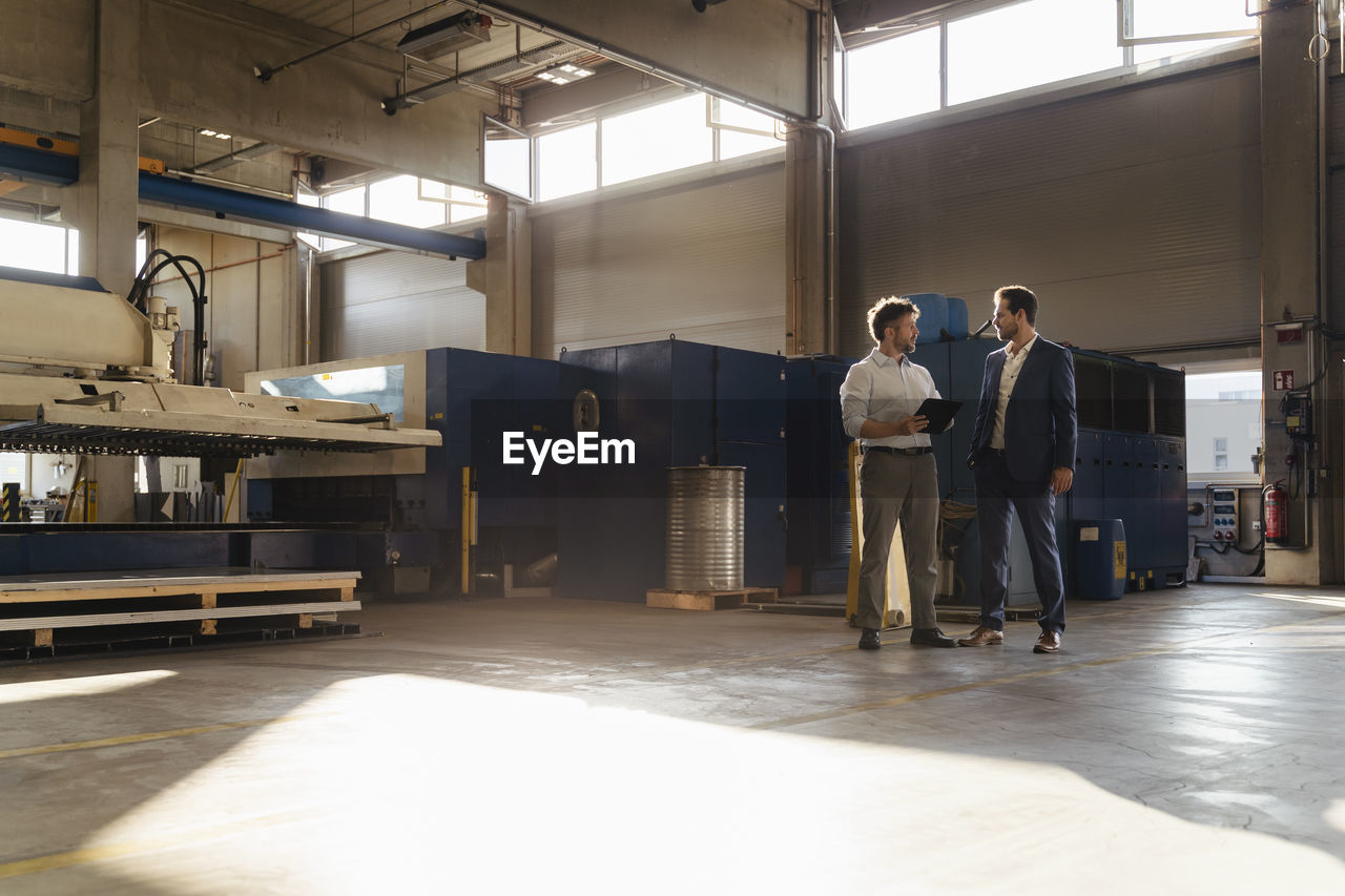 Businessman and colleague with digital tablet working while standing at factory