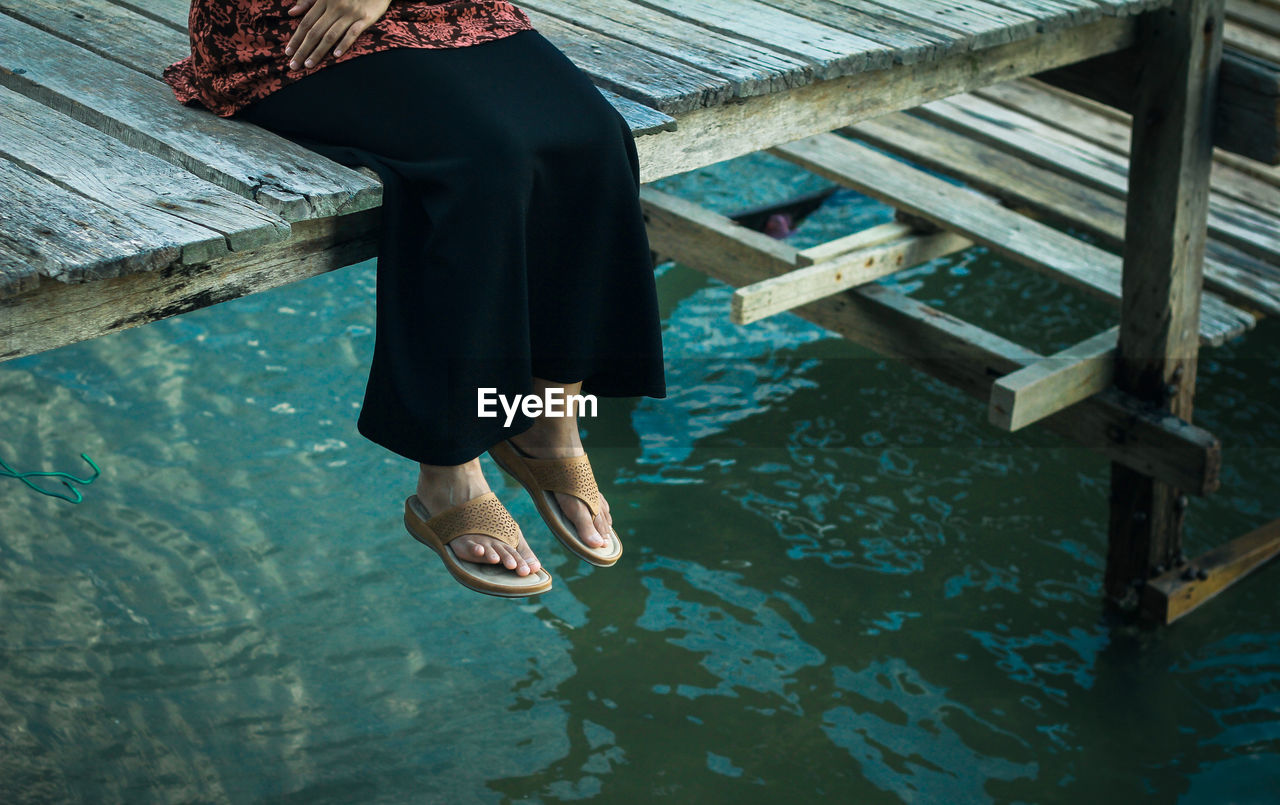 Low section of woman sitting on pier over lake