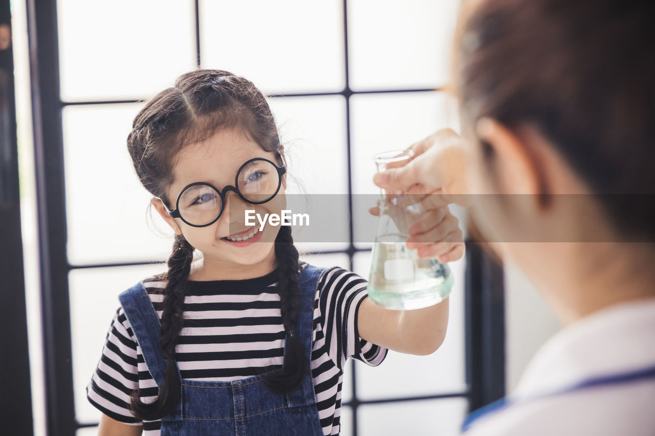 Smiling girl wearing glasses holding flask in laboratory