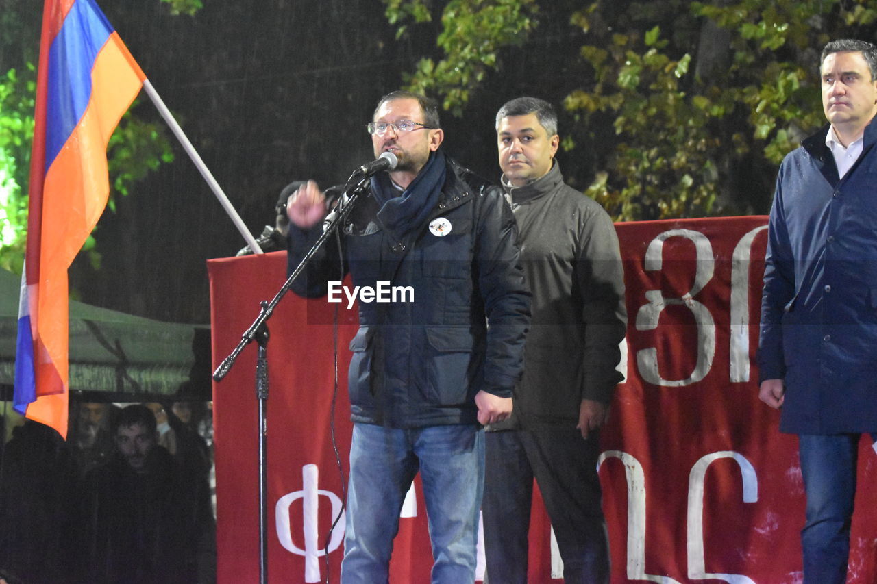 PORTRAIT OF A YOUNG MAN STANDING AGAINST PEOPLE