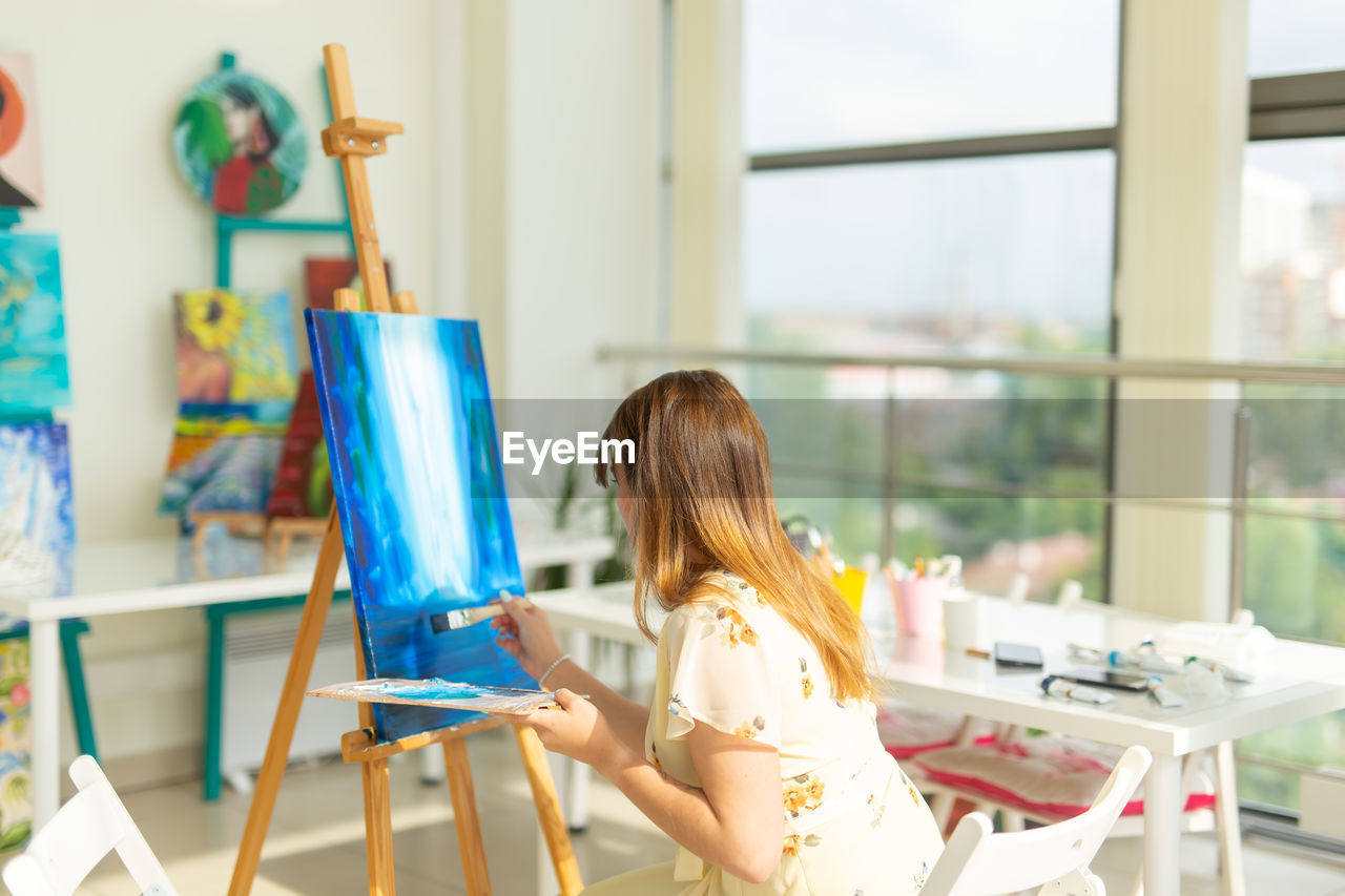 Rear view of young woman painting at home