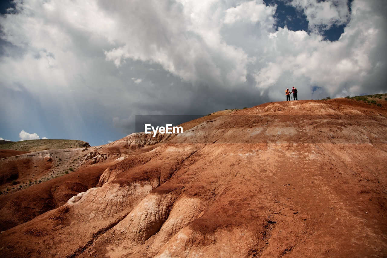 A man and a woman on the top of the red mountain against the sky