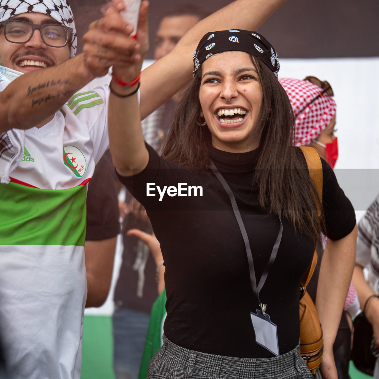 HAPPY YOUNG WOMAN STANDING AGAINST PEOPLE