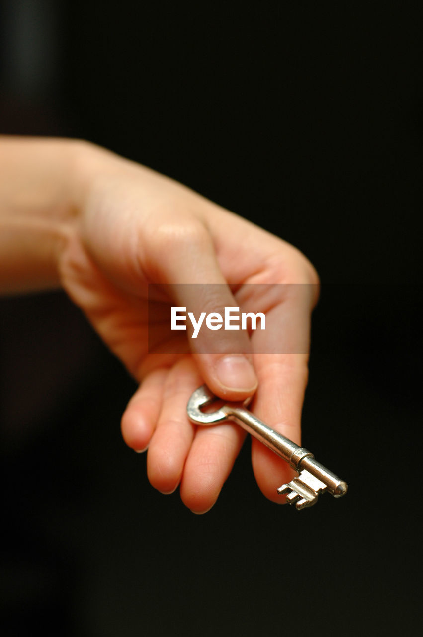 Cropped hand of woman holding key against black background