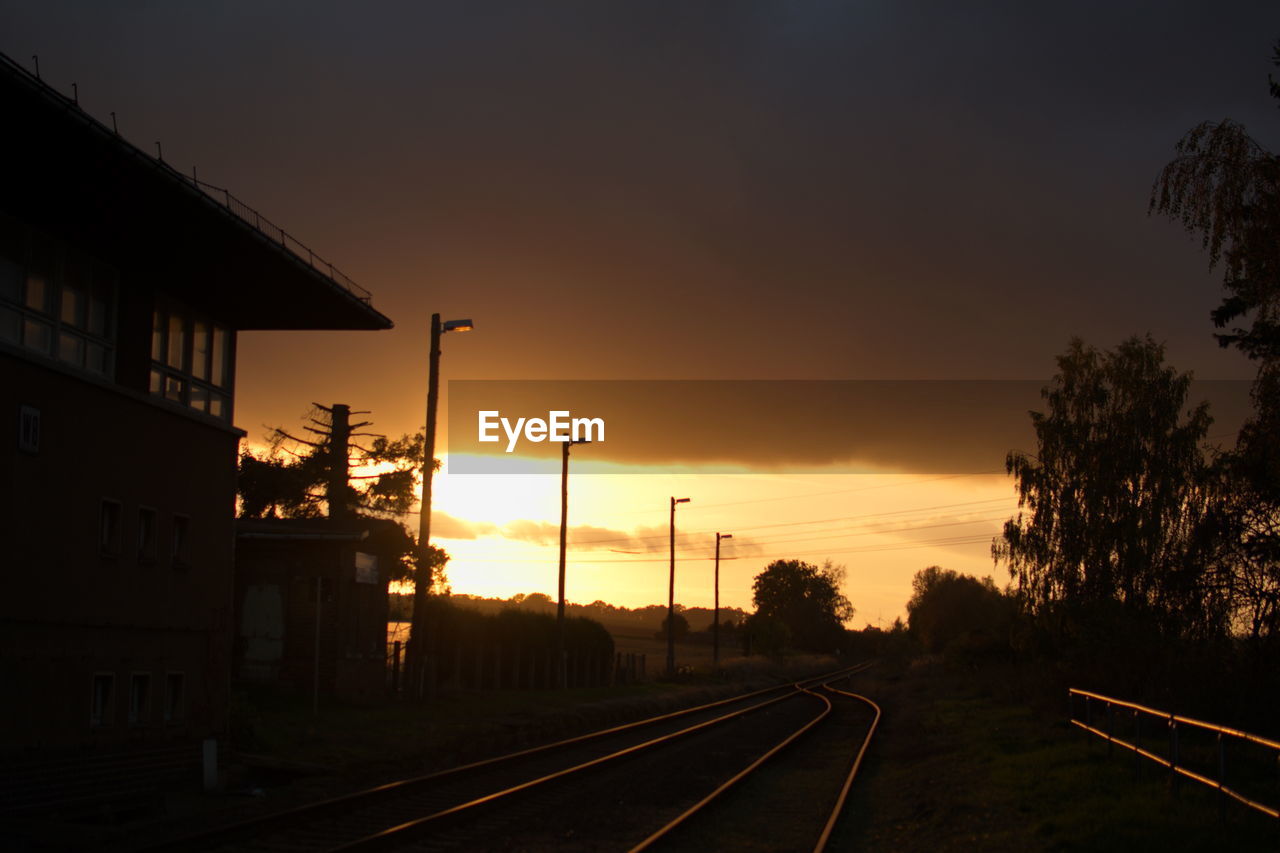 RAILROAD TRACKS BY TREES AGAINST SKY DURING SUNSET