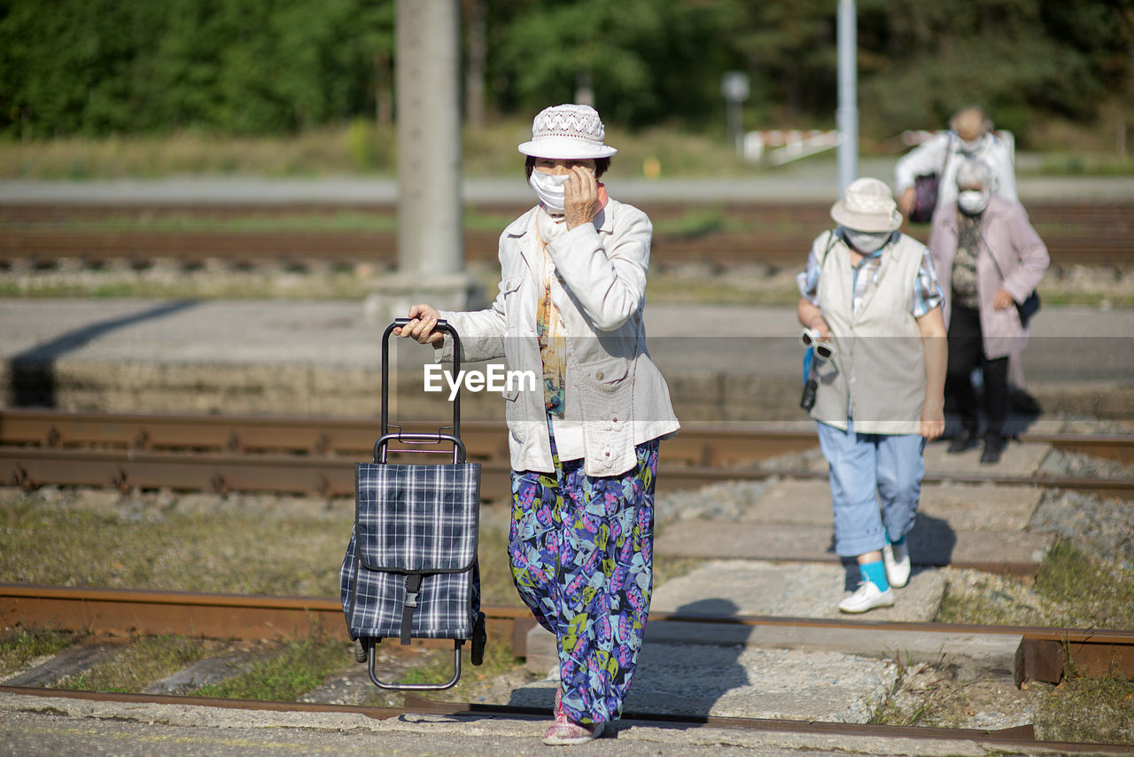 A group of senior travelers with masks on their faces cross the railway tracks